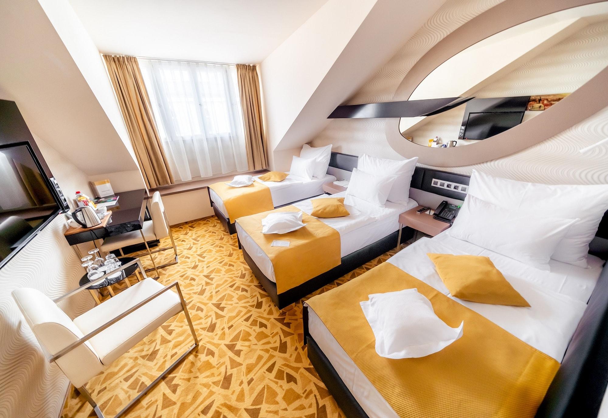 Grandium Hotel Prag Eksteriør billede The photo shows a hotel room featuring two twin beds, each made up with white linens and yellow decorative pillows. The room has a modern design with a light color scheme, including soft yellow tones. There's a large window letting in natural light, 