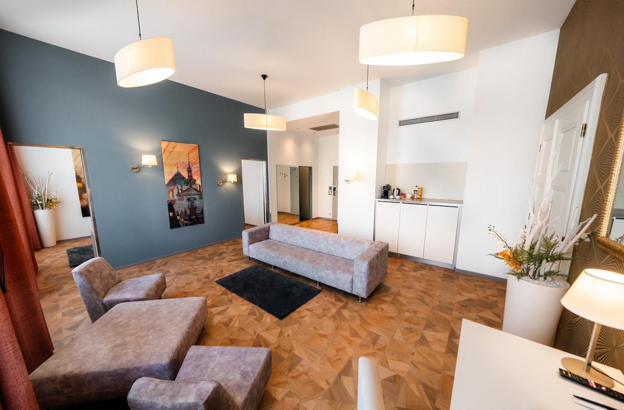 Grandium Hotel Prag Eksteriør billede The photo shows a modern and stylish living space. The room features light-colored walls and a distinct blue accent wall. There is a large, gray sectional sofa and a small black rug on the wooden floor. The space is well-lit with two pendant lamps ha
