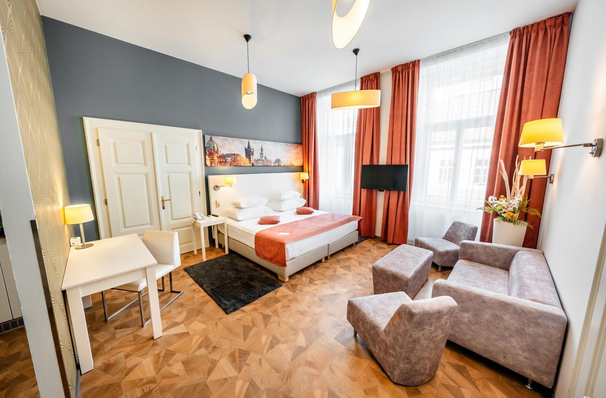 Grandium Hotel Prag Eksteriør billede The photo shows a stylish hotel room with a contemporary design. It features a double bed with a white and orange color scheme, accompanied by bedside lamps. There is a large window with sheer curtains that allows natural light to brighten the space.